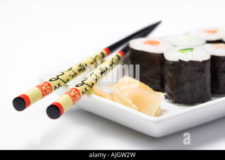Varie maki sushi rotoli, wasabi, zenzero e bastoncini su una bianca piastra rettangolare, prospettiva bassa Foto Stock