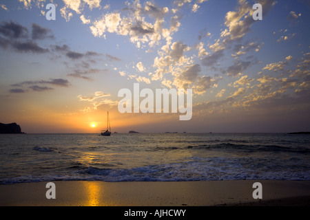 sunset seen from a beach at north-western coast of Ibiza, sailboat and rocky islands at horizon, interesting cloud formations Foto Stock