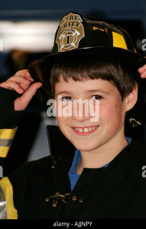 Ragazzo Fire Fighter in corrispondenza di un fuoco Fair vestito in uniforme come un incendio Chief Foto Stock