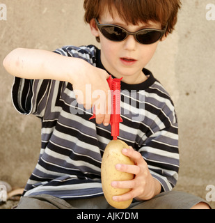 6 anno vecchio ragazzo seduto, giocando con una pistola spud durante le vacanze estive, indossando occhiali da sole Foto Stock