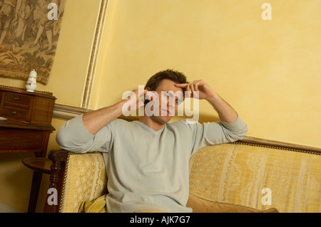 Uomo seduto su un divano mentre si parla al telefono alla ricerca riflessivo Foto Stock