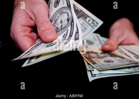 Un uomo con le mani su cinquanta le fatture del dollaro da un gran fascio di contanti in prossimità del raccolto di mani su sfondo nero Foto Stock