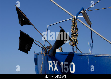 Pennarello nero bandiere appesa sopra la poppa di un blu pesca barca tirata sulla spiaggia a Hastings Foto Stock