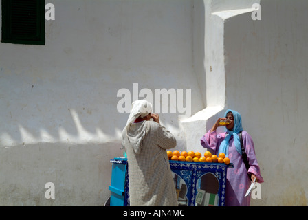 Due donne abbigliate in colorate djellabahs bere il succo d'arancia appena spremuto da un piccolo box nella Medina. Foto Stock