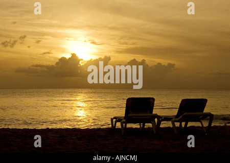 Due sedie a sdraio su un vuoto spiaggia caraibica durante un tramonto Foto Stock