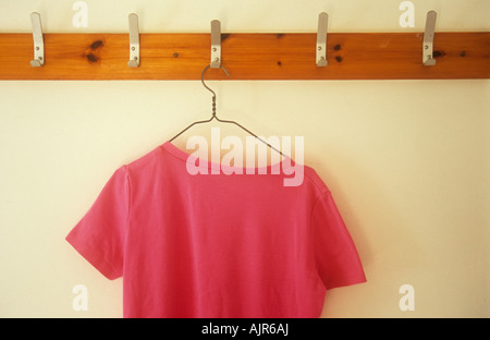T-shirt rosa sul filo appendiabiti appesi da gancio in metallo in fila di vestiti ganci montati su legno sulla parete di crema Foto Stock
