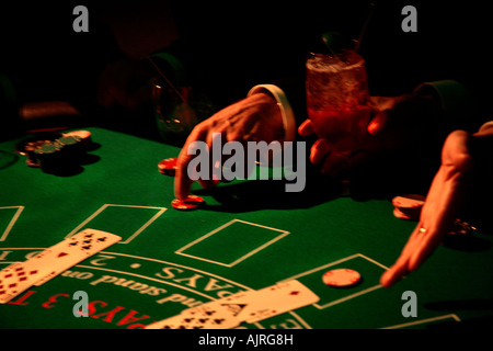 Il gioco d'azzardo, giochi Black Jack tabella scheda saldamente con le mani tagliate che puntano a chip, dicendo " Hit me', una mano trattiene un drink. Casino di Las Vegas Foto Stock