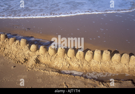 Fila di quindici Il Sandcastles On spiaggia sabbiosa in procinto di essere sommersi dalla marea Foto Stock