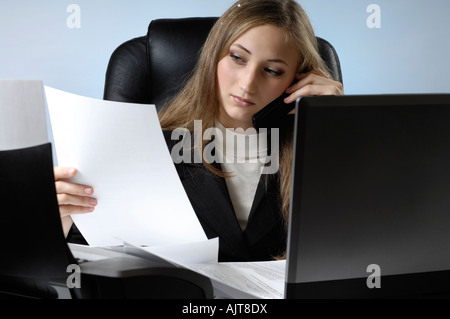 Giovane imprenditrice lavoro in ufficio con una carta di tutto il desk a parlare su un telefono cellulare e la lettura di un documento Foto Stock