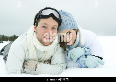 Coppia giovane affiancati in snow, sorridente in telecamera, ritratto Foto Stock