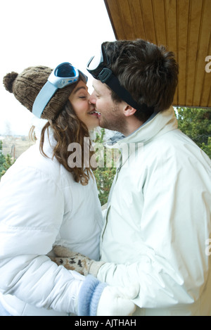 Coppia giovane kissing, faccia a faccia, vestito in abiti invernali, vista laterale Foto Stock