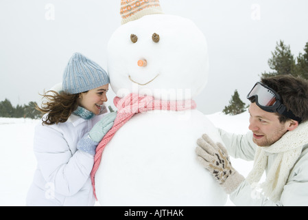 Due giovani amici peeking pupazzo di neve intorno a ciascun altro, sorridente Foto Stock
