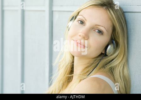 Giovane donna ascoltando le cuffie, sorridente in telecamera, ritratto Foto Stock