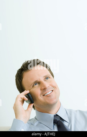 Imprenditore tramite telefono cellulare, sorridente, guardando in alto, ritratto Foto Stock
