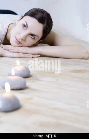 Giovane donna sdraiata su stomaco, testa in appoggio sui bracci, candele accese in primo piano Foto Stock