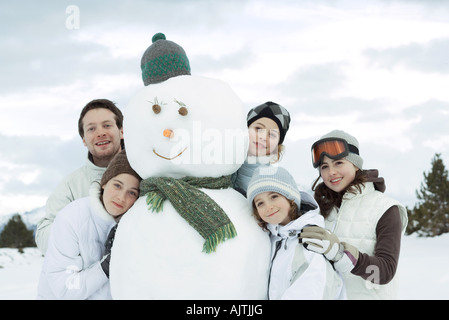 Un gruppo di giovani amici riuniti intorno al pupazzo di neve Foto Stock