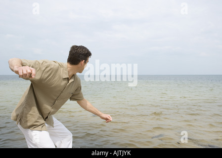 Uomo in bilico per scremare pietra sulla superficie dell oceano, vista laterale, tre quarti di lunghezza Foto Stock