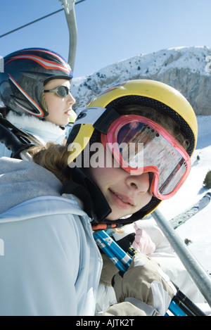 Due giovani sciatori sulla seggiovia, una sorridente in telecamera Foto Stock