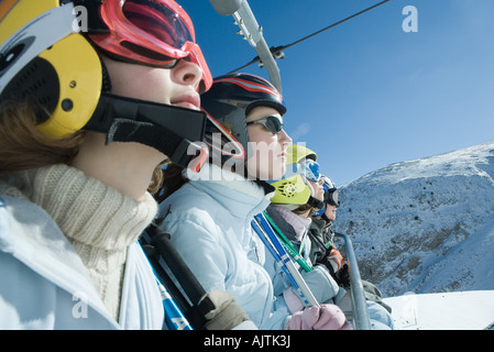 Quattro giovani sciatori sulla seggiovia, guardando lontano, vista laterale Foto Stock