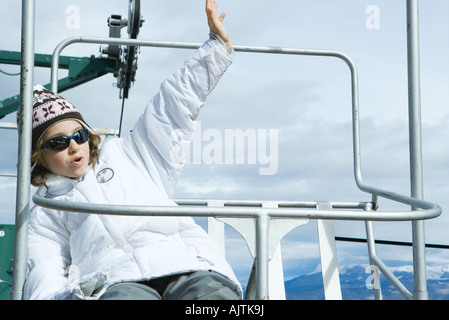 Ragazza seduta su una sedia di sollevamento, agitando, guardando lontano Foto Stock