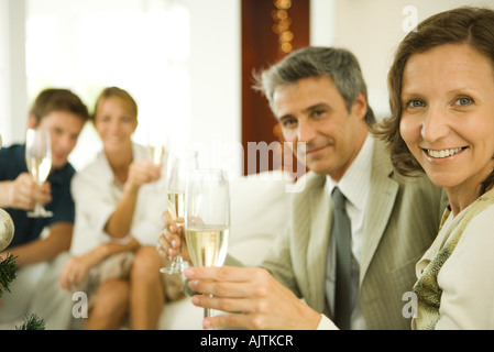 Giovane fare un brindisi con champagne, sorridente in telecamera, amici in background Foto Stock