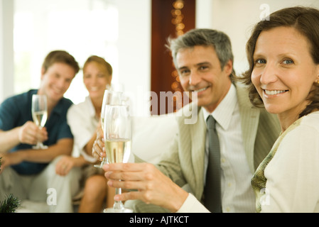 Giovane fare un brindisi con champagne, sorridente in telecamera, amici in background Foto Stock