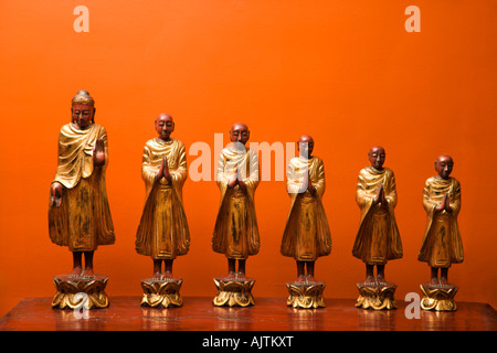 Statue in legno del Buddha con cinque discepoli contro la parete arancione Foto Stock