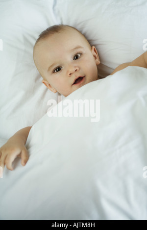 Il bambino nel letto sotto il piumone, guardando la telecamera, ad alto angolo di visione Foto Stock