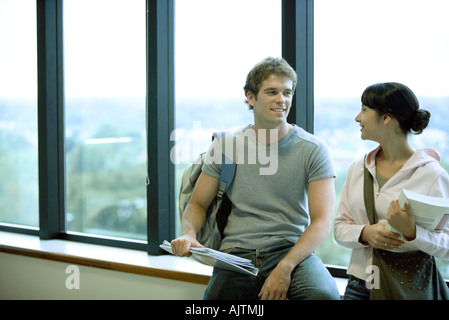Maschio e femmina di studenti del college, appoggiata contro la finestra chat Foto Stock