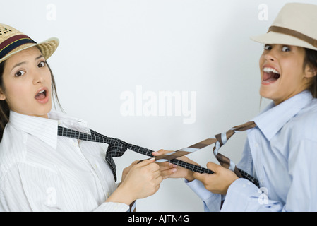 Due giovani amici di sesso femminile vestito di cappelli, tirando reciprocamente le cravatte, guardando la fotocamera Foto Stock