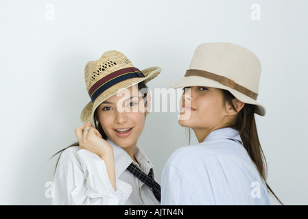 Due giovani amici di sesso femminile di indossare cappelli e cravatte, sorridente in telecamera, uno guardando sopra la spalla Foto Stock