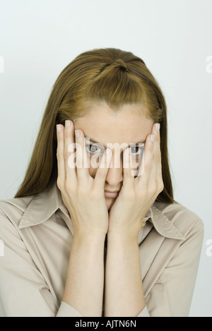 Giovane donna che guarda la fotocamera e le mani sulla faccia, ritratto Foto Stock