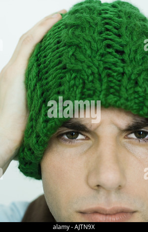 Giovane uomo che indossa knit hat, guardando la telecamera, solcando brow Foto Stock