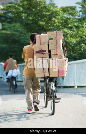 Uomo che cammina con la bici impilati con scatole Foto Stock