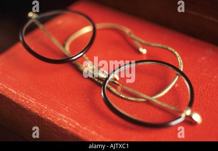 Un paio di occhiali con lenti circolari e sottili trame tartaruga e filo bracci giacenti su un libro rosso Foto Stock