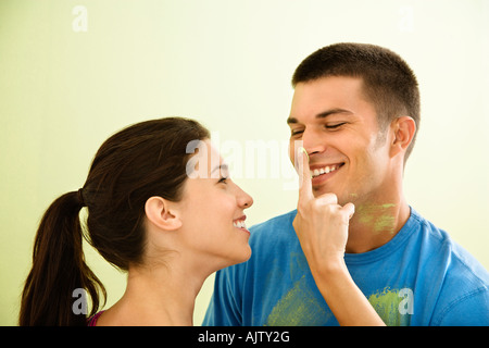 Giocoso donna sorridente mettendo la vernice sull'uomo s naso Foto Stock