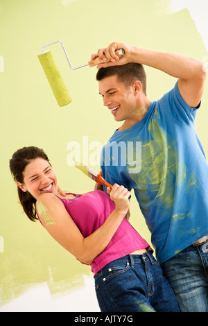 Coppia attraente in piedi di fronte a parzialmente parete dipinta scherzosamente mettendo la vernice sulla vicenda Foto Stock