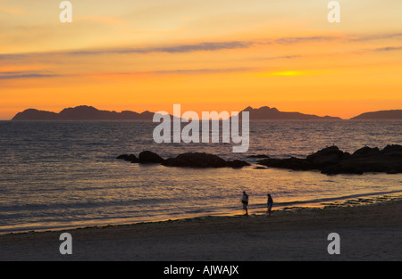 Walkers sul galiziano Playa de Samil spiaggia al tramonto Cies isola in background Spagna Foto Stock