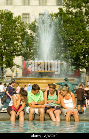 Ritratto verticale di turisti il raffreddamento con i piedi nelle fontane a Trafalgar Square in un caldo giorno d'estate. Foto Stock