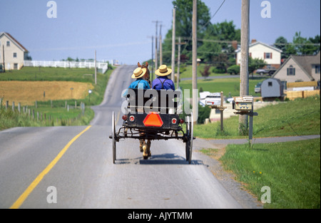 Un agricoltore Amish e suo figlio aziona il suo cavallo e carro lungo una strada in città nei pressi della sua azienda agricola Foto Stock