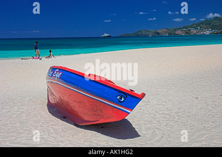 Barca da pesca rossa e blu su sabbie dorate di spiaggia con mare turchese blu cielo montagne sullo sfondo, Grenada Foto Stock