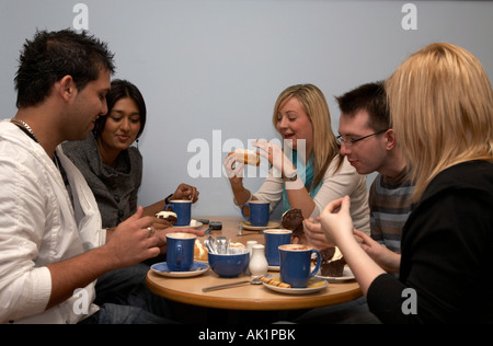 Il gruppo di cinque razza mista gli studenti seduti in un caffè gustando una tazza di caffè e alcune focacce Foto Stock