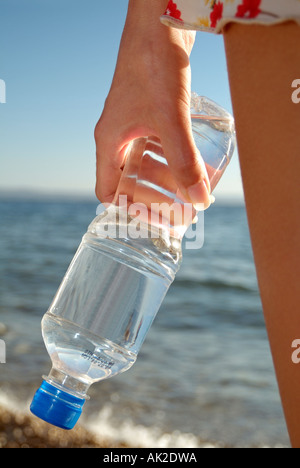 Giovane donna in possesso di una bottiglia di acqua minerale sulla spiaggia sulla sezione centrale stretta fino Foto Stock