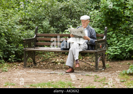 Un vecchio uomo la lettura di un quotidiano in un parco Foto Stock