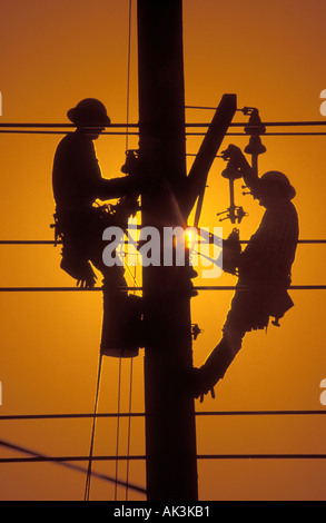 Silouetted contro un pomeriggio di sole due linemen elettrico opera su un polo utilità a Irvine California USA Foto Stock