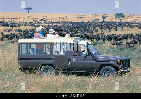 Toyota Landcruiser su un game drive attraverso grandi mandrie di gnu che pascolano nella Riserva Nazionale di Masai Mara Kenya Foto Stock