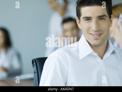 Imprenditore sorridente alla fotocamera, i colleghi in background, ritratto Foto Stock