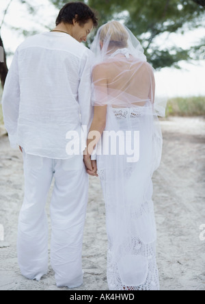 Sposa e lo sposo camminando sulla spiaggia, tenendo le mani, vista posteriore Foto Stock