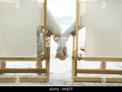 Giovane seduto in spiaggia, sedie, tenendo le mani, vista posteriore Foto Stock