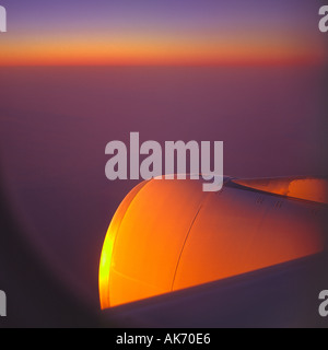 Vista dall'aereo di linea di passeggeri battenti finestra a trenta mila piedi di sunrise che riflette i colori arancio luminoso rosso sul motore a getto Foto Stock